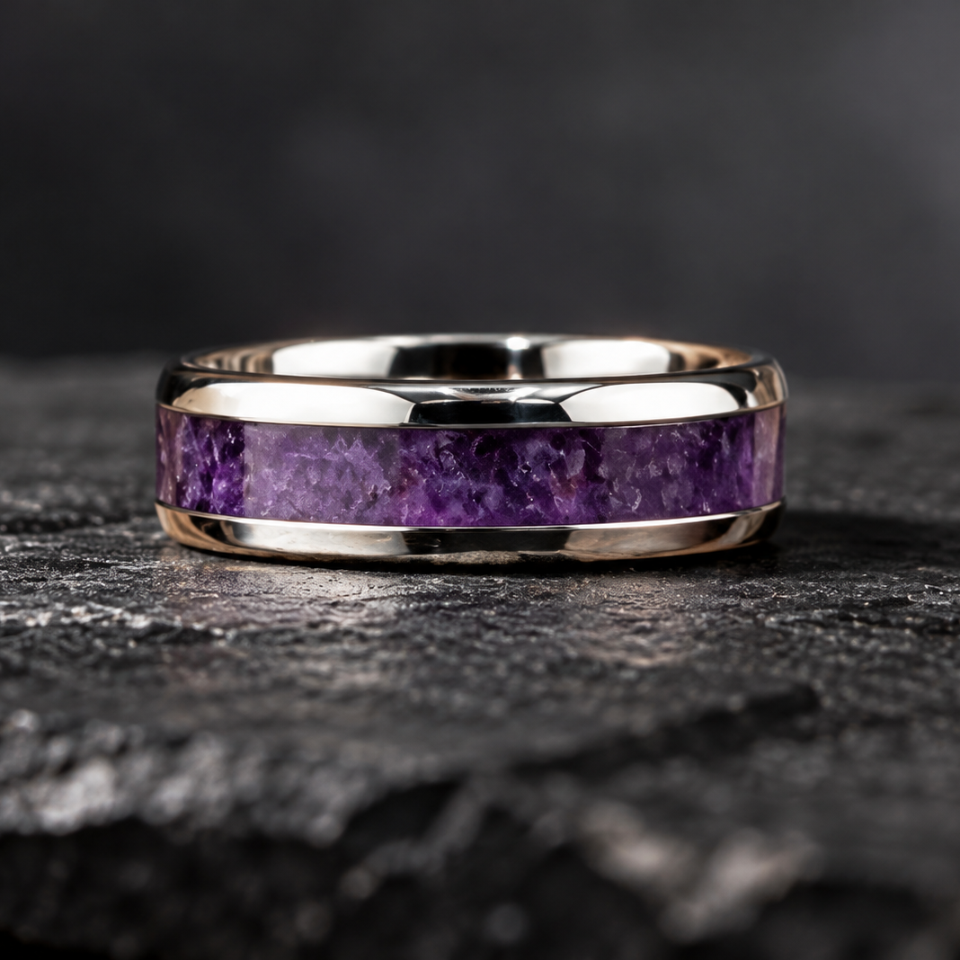 A polished silver band ring featuring a textured purple amethyst inlay, displayed on a dark, textured stone surface.