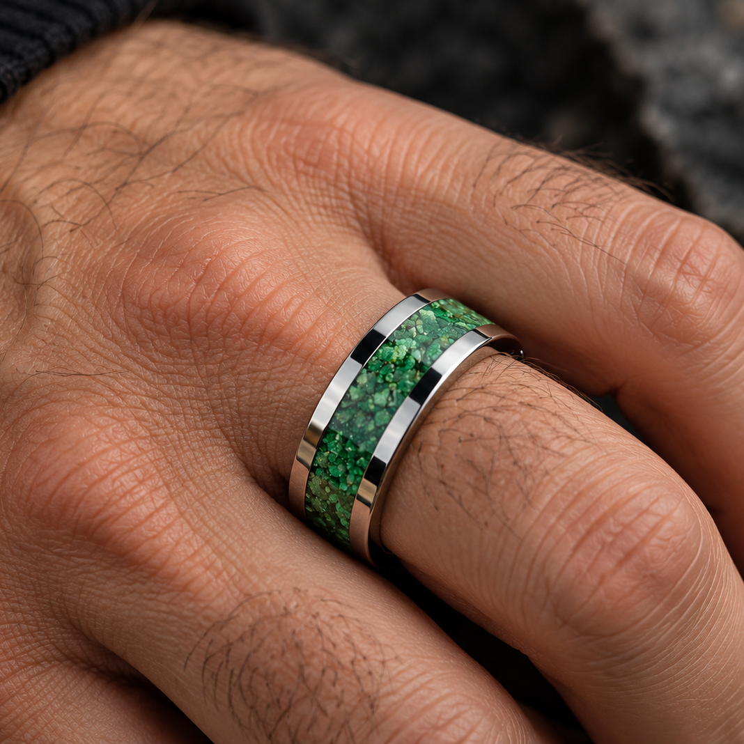 A close-up of a hand wearing a silver band ring with a vibrant green inlay featuring a textured, stone-like pattern.