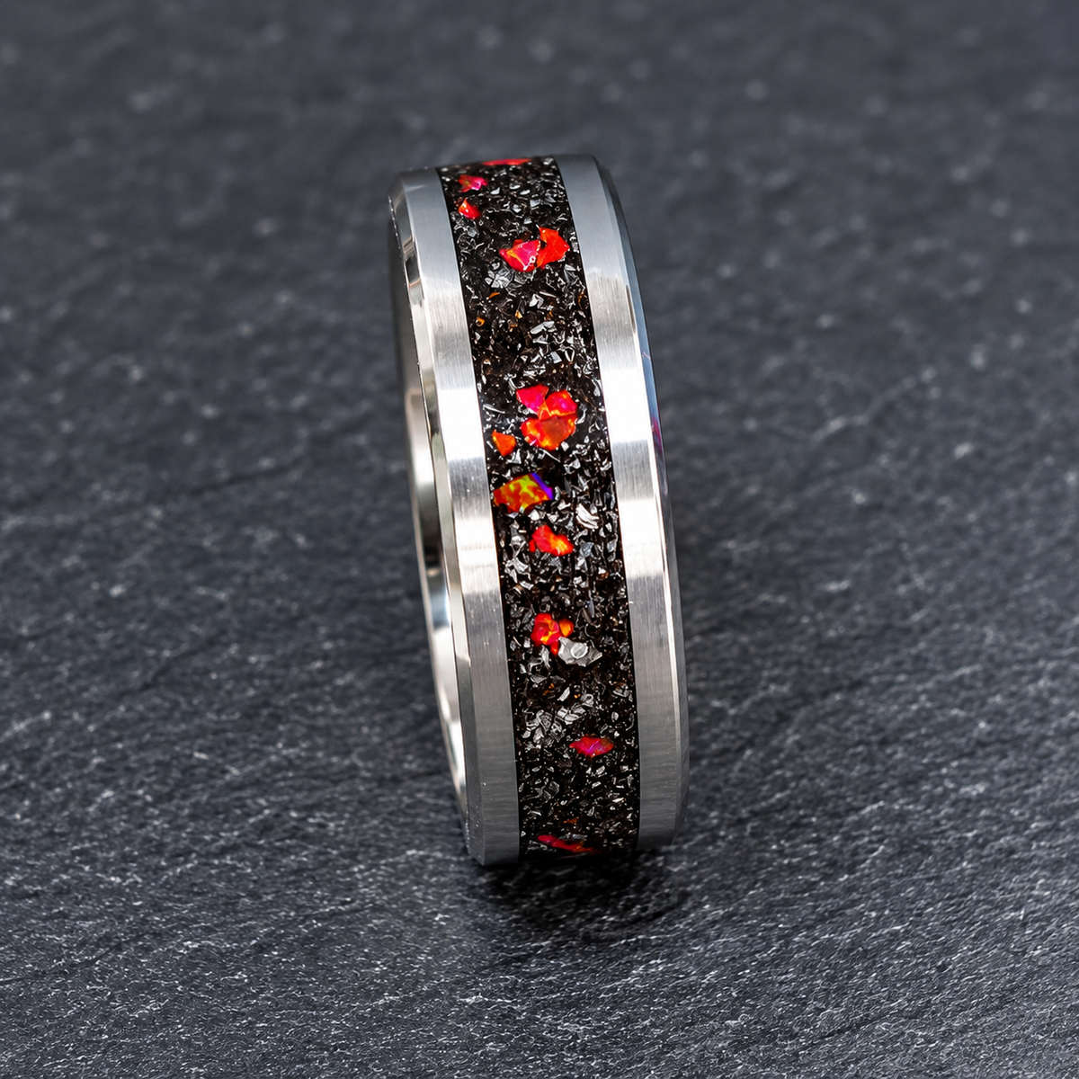 A silver-toned band ring featuring a central inlay of black chert filled with colorful iridescent opal flecks, set against a dark textured slate background.
