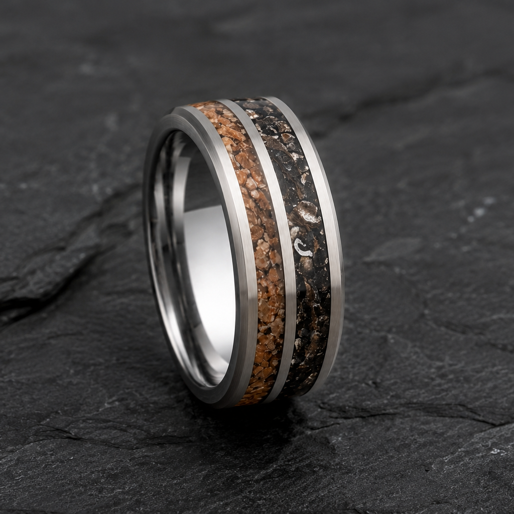 A polished silver-toned ring with two inlay stripes, one featuring a black-and-brown speckled pattern and the other a warm copper-brown speckled pattern, displayed on a dark textured slate surface.