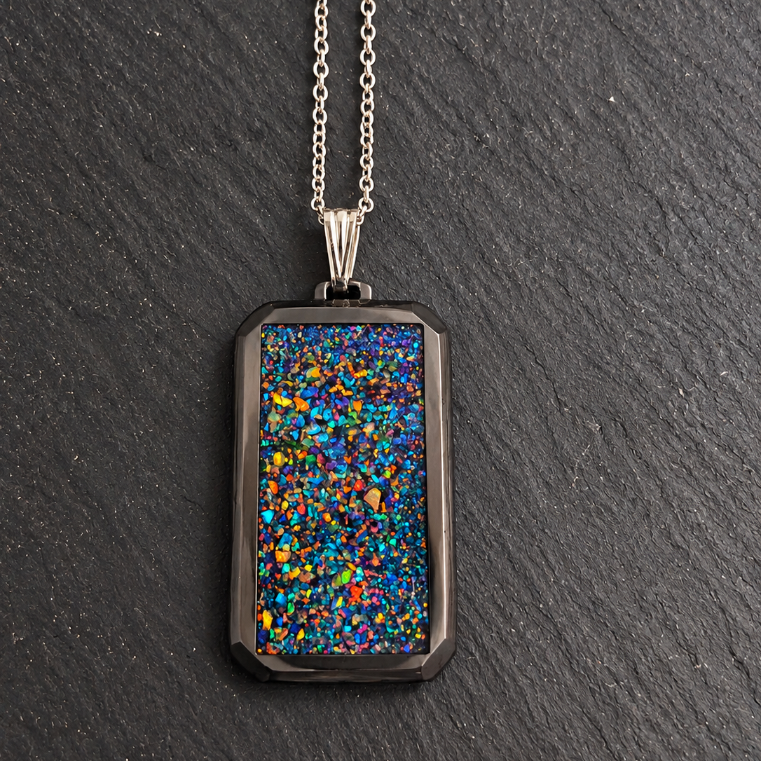 A silver-toned necklace with a rectangular pendant featuring a vibrant, multicolored opal inlay, displayed on a dark slate background.