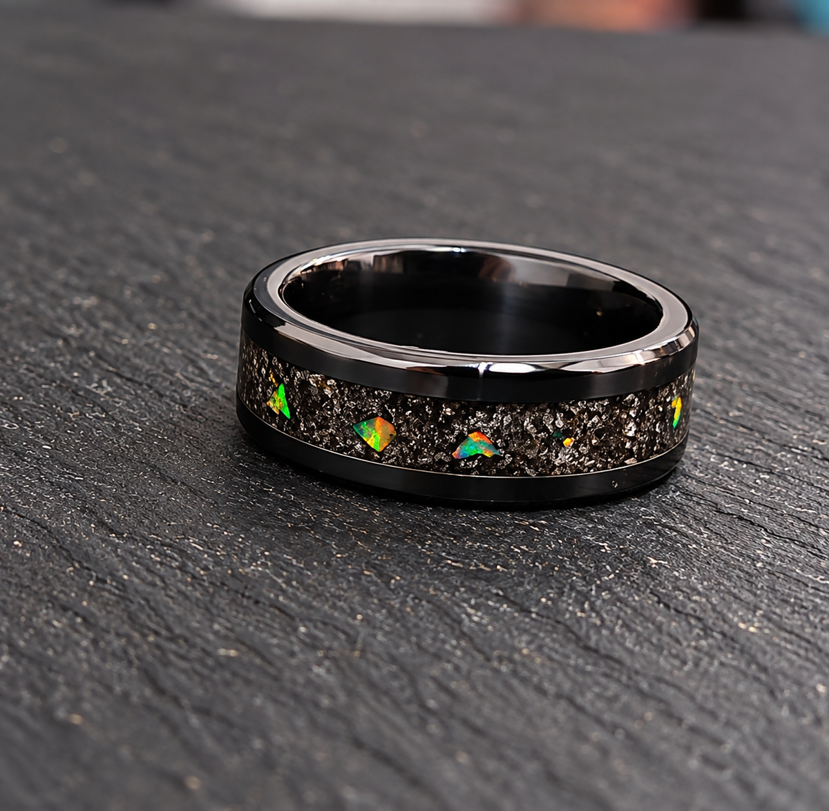 A black ceramic ring with a textured inlay of small iridescent opal-like stones, resting on a dark textured slate surface.