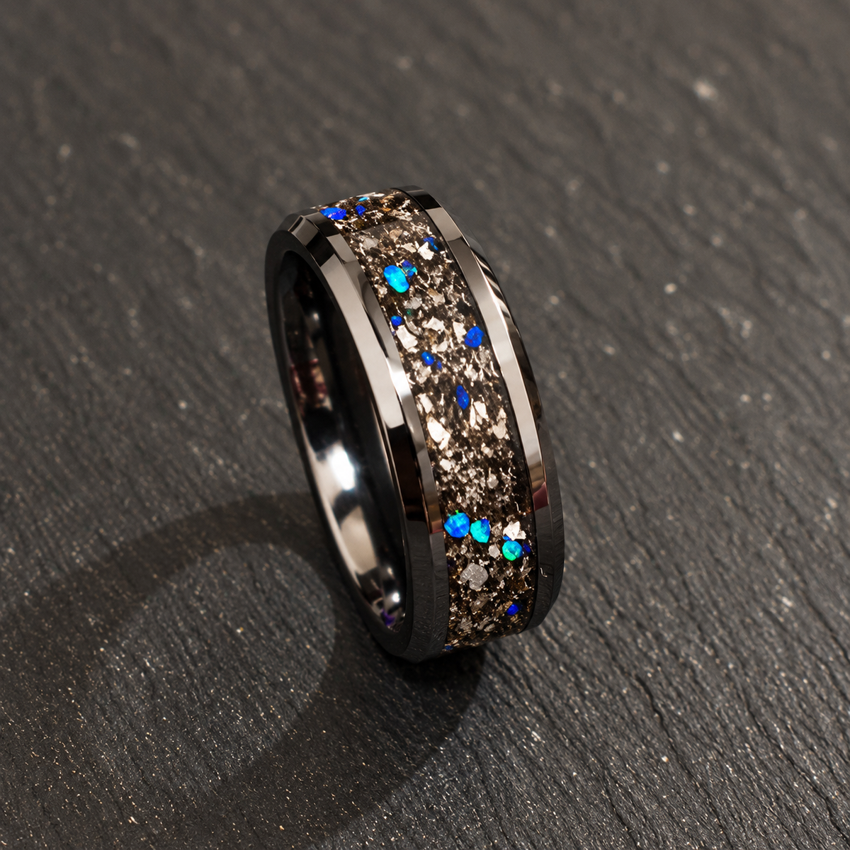 A dark metallic band ring with a textured, glittery brown center channel accented by scattered blue and turquoise rhinestones, resting on a dark gray textured surface.