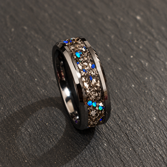 A dark metallic band ring with a textured, glittery brown center channel accented by scattered blue and turquoise rhinestones, resting on a dark gray textured surface.