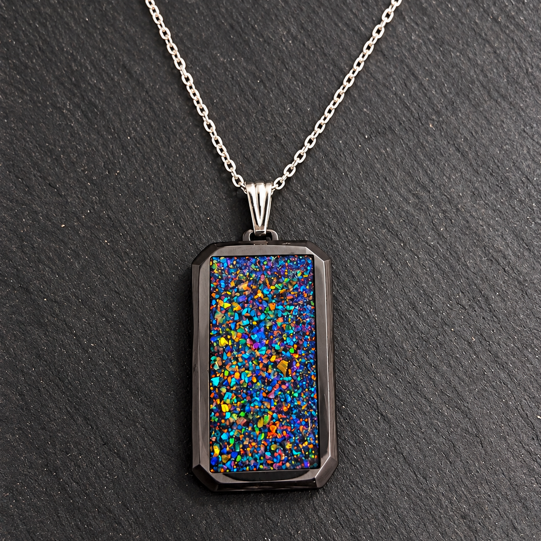 A silver-toned chain necklace with a rectangular pendant featuring a dark, textured opal-like inlay that displays vibrant multicolor flashes of blue, green, orange, and yellow, set against a dark slate background.