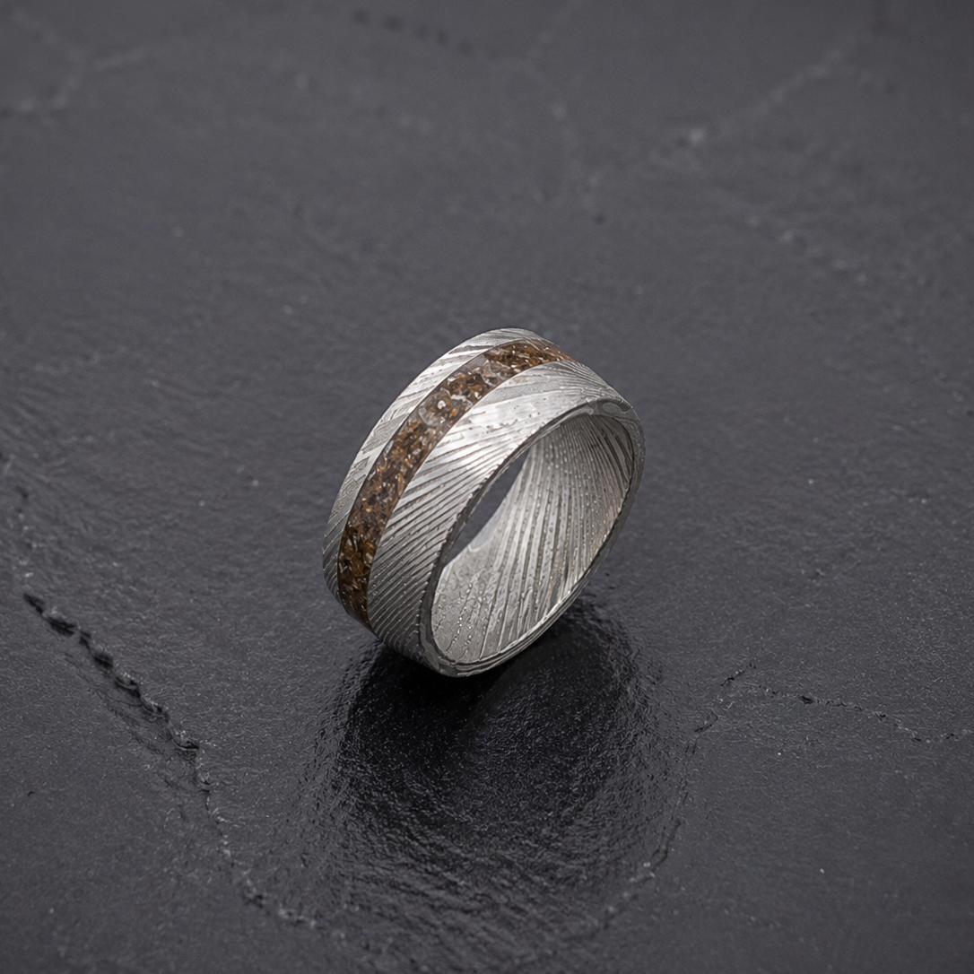 A silver ring with a textured, wavy pattern and a central inlay of brown Dinosaur Bone, displayed on a dark slate surface.